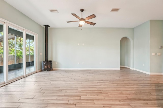 unfurnished room with arched walkways, a wood stove, light wood-style flooring, and visible vents