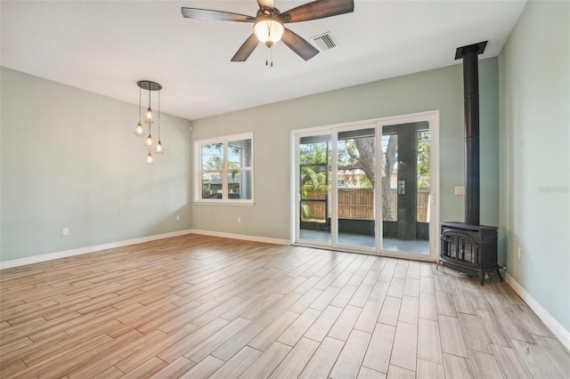 unfurnished room featuring light wood finished floors, baseboards, visible vents, a ceiling fan, and a wood stove