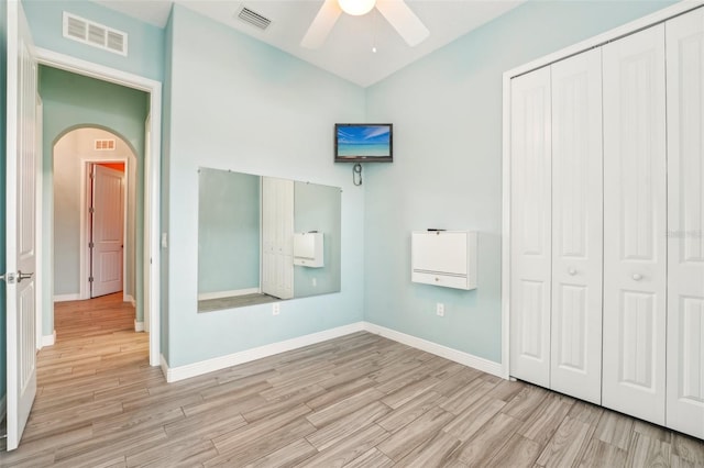 unfurnished bedroom with visible vents, arched walkways, a closet, and wood finished floors