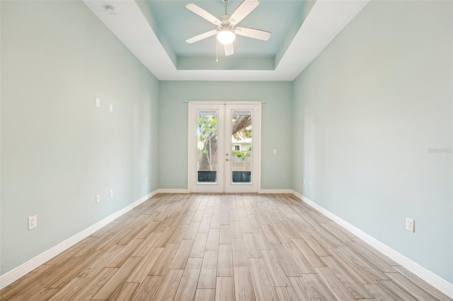 empty room with french doors, a raised ceiling, light wood-style floors, ceiling fan, and baseboards