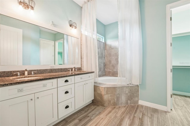 bathroom with double vanity, a relaxing tiled tub, a sink, and baseboards