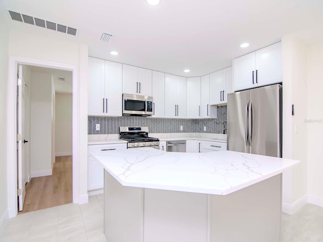 kitchen featuring light stone countertops, stainless steel appliances, white cabinets, and a kitchen island