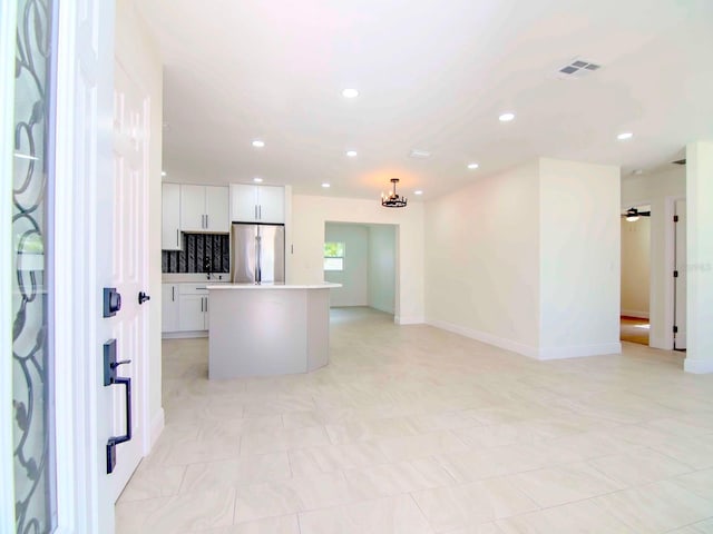 kitchen with stainless steel fridge, ceiling fan, white cabinets, a kitchen island, and decorative light fixtures