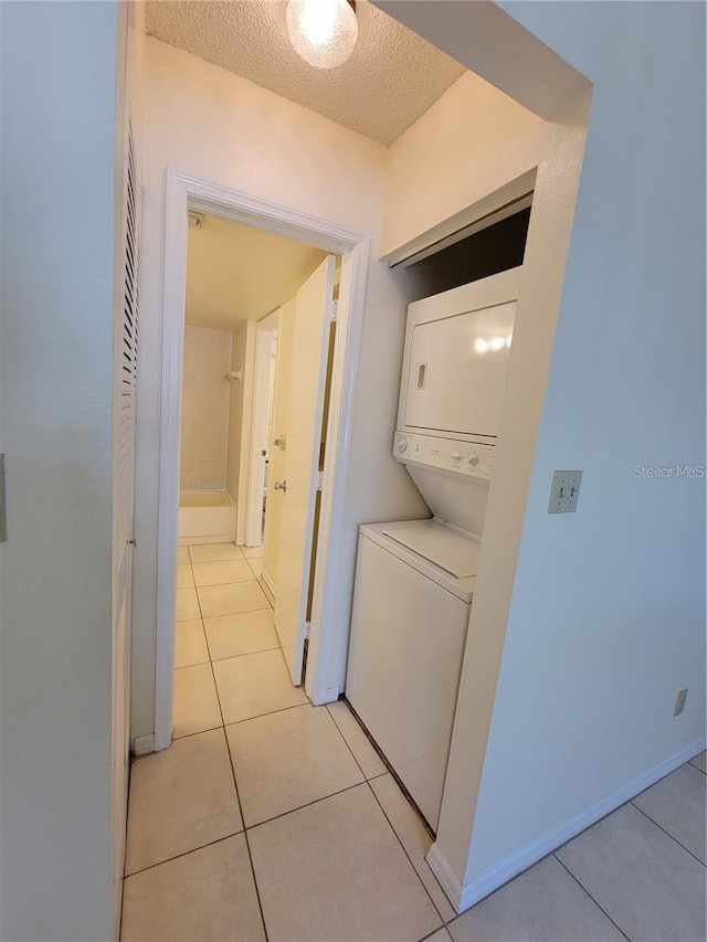 laundry room featuring light tile patterned floors, a textured ceiling, and stacked washer / drying machine