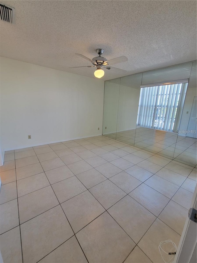 spare room featuring ceiling fan, light tile patterned flooring, and a textured ceiling