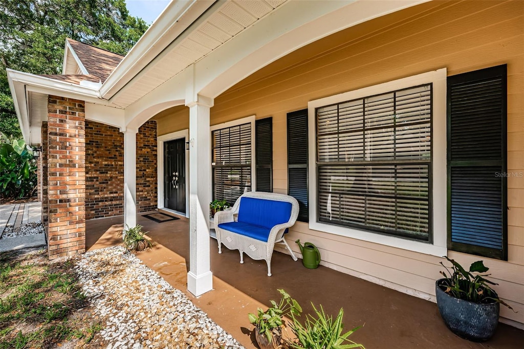 view of exterior entry featuring covered porch, brick siding, and roof with shingles