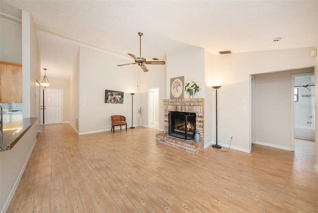 unfurnished living room with visible vents, ceiling fan, light wood-style floors, a fireplace, and high vaulted ceiling