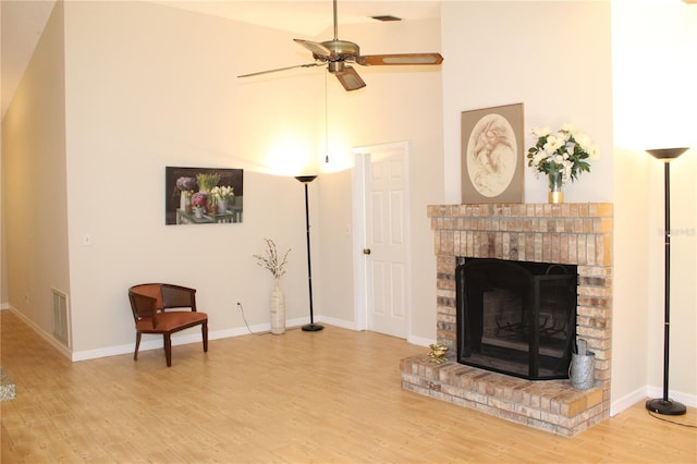 living area with a brick fireplace, baseboards, visible vents, and wood finished floors