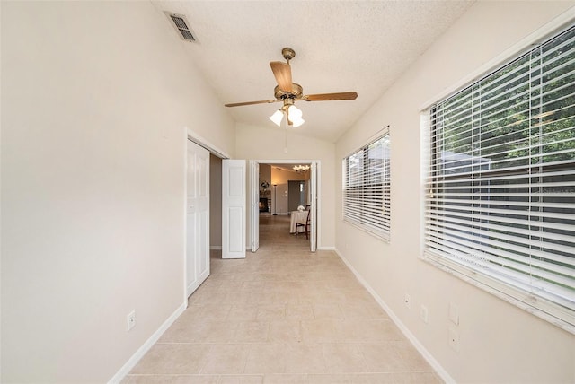 hallway with baseboards, visible vents, vaulted ceiling, and a textured ceiling