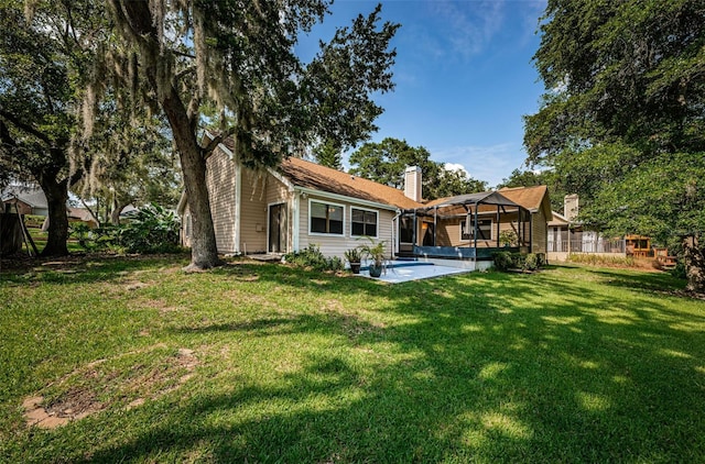 back of house featuring a chimney, a lawn, and a patio