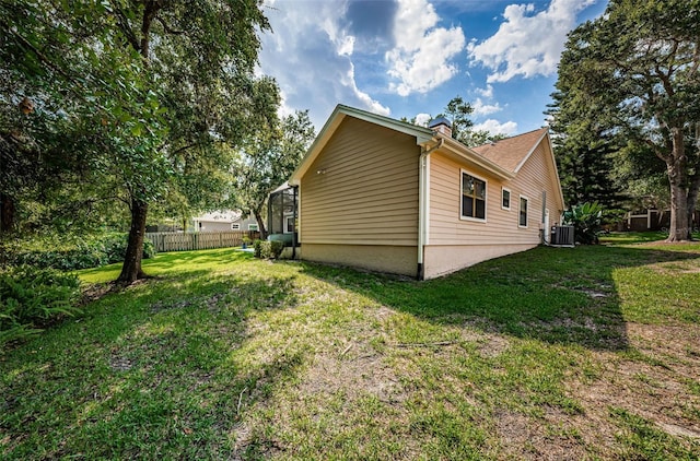 view of side of property with a lawn, fence, and central AC unit