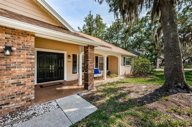 entrance to property with roof with shingles, a porch, and brick siding