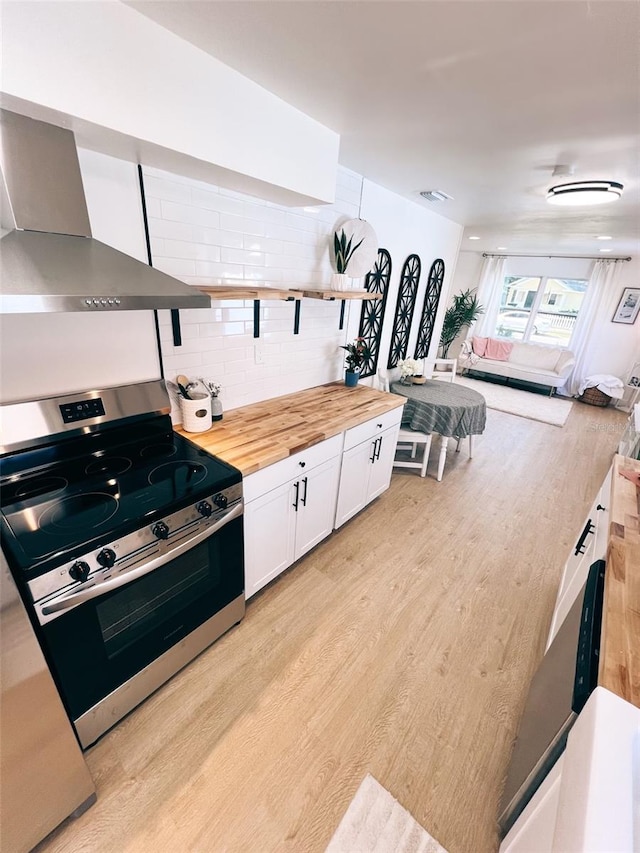 kitchen featuring stainless steel electric range oven, white cabinetry, wooden counters, light hardwood / wood-style floors, and wall chimney exhaust hood