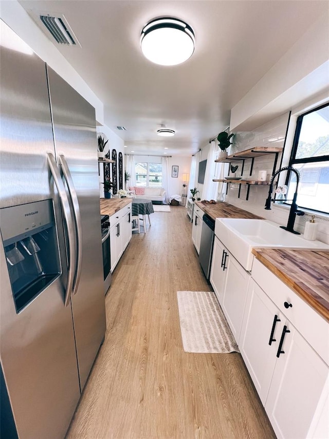 kitchen with white cabinetry, appliances with stainless steel finishes, sink, and butcher block countertops