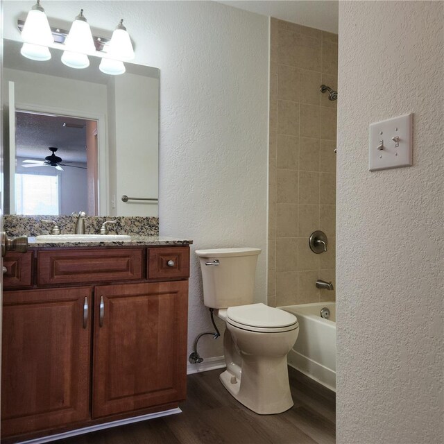 full bathroom with ceiling fan, hardwood / wood-style floors, vanity, tiled shower / bath, and toilet