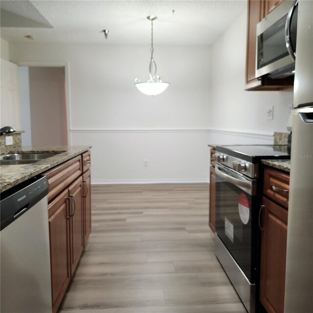 kitchen featuring sink, light stone counters, decorative light fixtures, appliances with stainless steel finishes, and light hardwood / wood-style floors