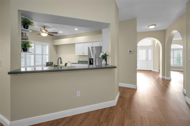 kitchen with white cabinetry, kitchen peninsula, stainless steel fridge with ice dispenser, and a healthy amount of sunlight