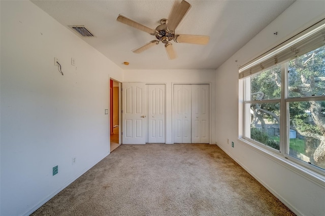 unfurnished bedroom with carpet floors, multiple windows, and multiple closets