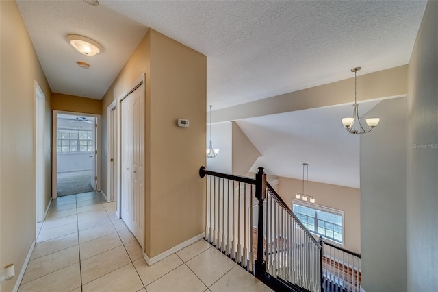 corridor featuring light tile patterned floors, a textured ceiling, and an inviting chandelier