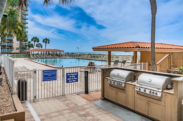 view of patio featuring a water view, grilling area, a community pool, and exterior kitchen