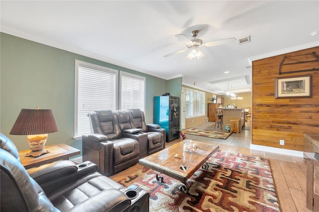 living room with wooden walls, light wood-type flooring, ceiling fan with notable chandelier, and ornamental molding