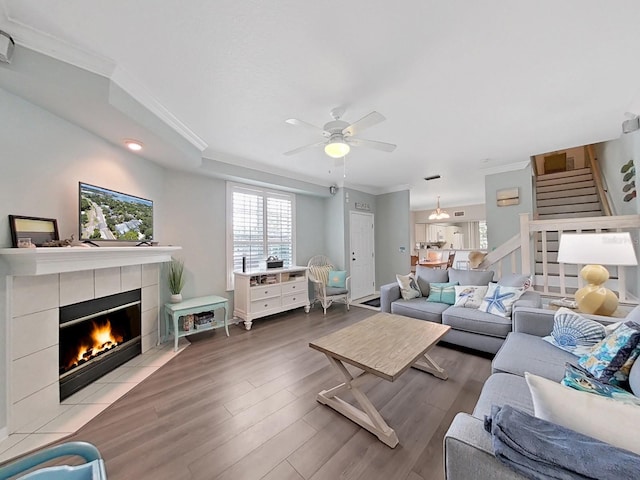 living room featuring hardwood / wood-style floors, ceiling fan, ornamental molding, and a tile fireplace