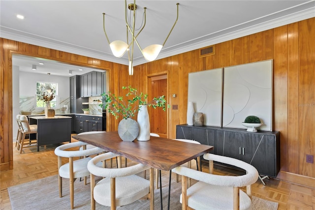 dining space with a notable chandelier, crown molding, wooden walls, and light parquet floors