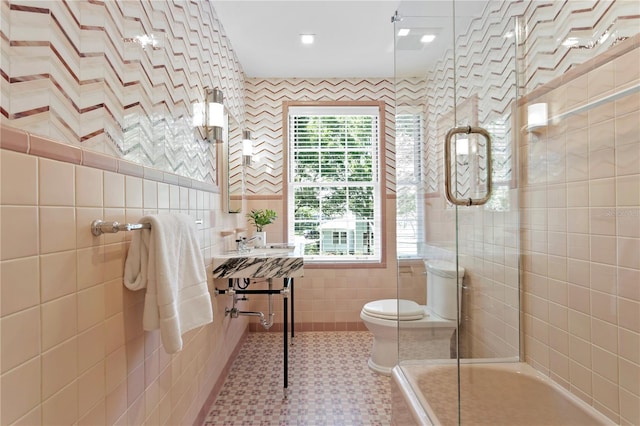 bathroom with toilet, an enclosed shower, tile patterned flooring, and tile walls