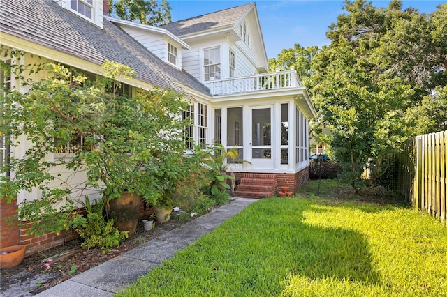 rear view of property featuring a balcony, a yard, and a sunroom