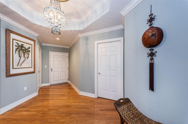 entrance foyer featuring an inviting chandelier, ornamental molding, light wood-type flooring, and a raised ceiling