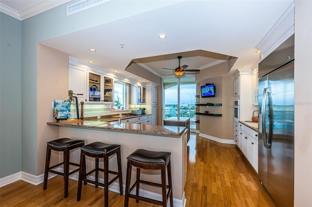 kitchen with light hardwood / wood-style floors, kitchen peninsula, stainless steel appliances, a breakfast bar area, and white cabinetry