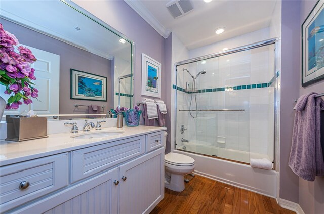 full bathroom featuring crown molding, hardwood / wood-style floors, enclosed tub / shower combo, vanity, and toilet