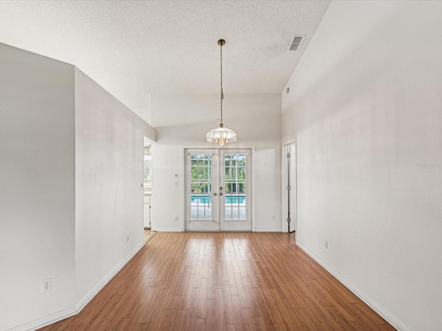 empty room with hardwood / wood-style flooring, french doors, a textured ceiling, and an inviting chandelier