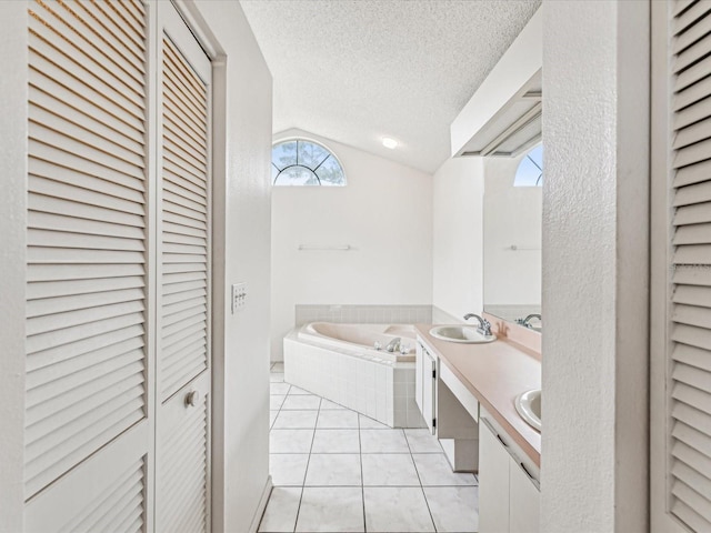 bathroom featuring vanity, a textured ceiling, vaulted ceiling, tiled tub, and tile patterned flooring