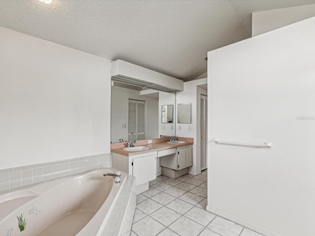 bathroom with tile patterned floors, vanity, a textured ceiling, vaulted ceiling, and tiled tub