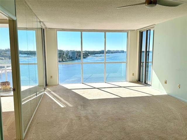 unfurnished room with ceiling fan, a water view, and expansive windows