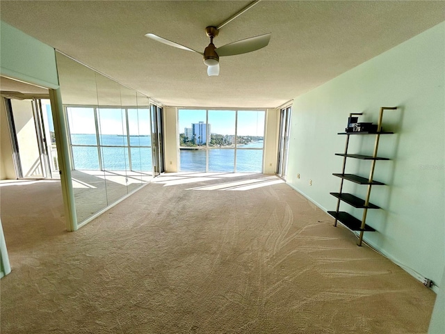 carpeted spare room with a wall of windows, a textured ceiling, ceiling fan, and a water view