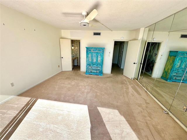 unfurnished bedroom with light colored carpet, ceiling fan, a textured ceiling, and a closet