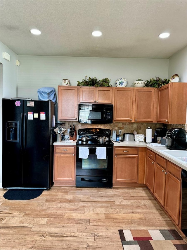 kitchen featuring light hardwood / wood-style floors, sink, black appliances, and decorative backsplash