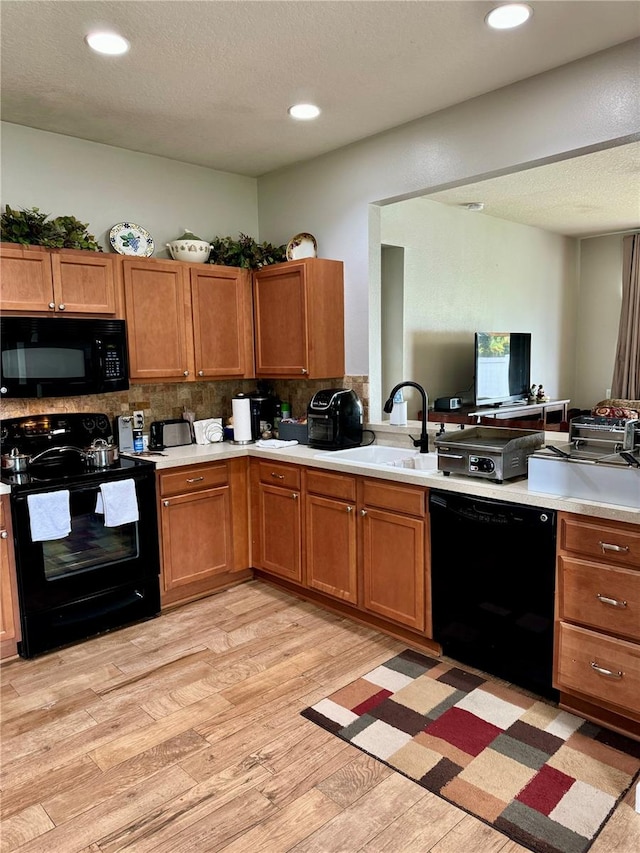 kitchen with decorative backsplash, sink, light wood-type flooring, and black appliances