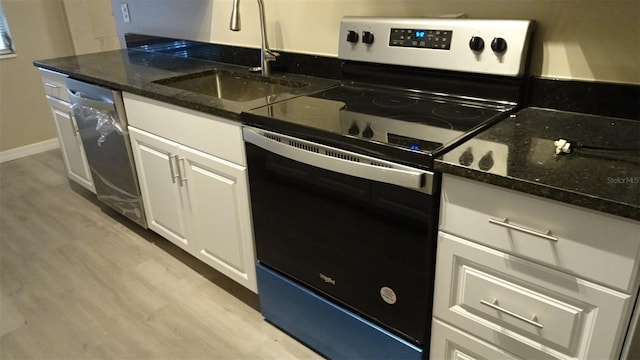 kitchen featuring a sink, stainless steel appliances, dark stone counters, white cabinets, and light wood finished floors