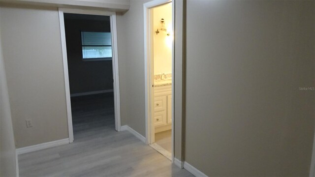 corridor with a sink, light wood-type flooring, and baseboards