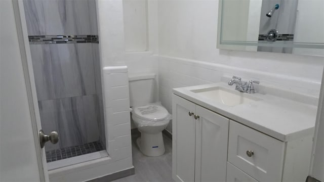 full bath featuring toilet, a stall shower, tile walls, wainscoting, and vanity