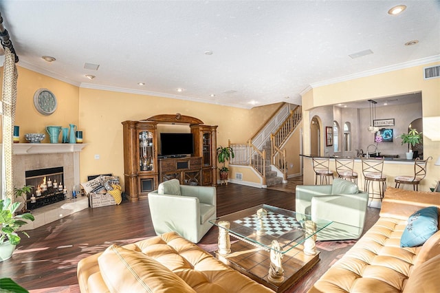 living room with sink, a tiled fireplace, ornamental molding, and hardwood / wood-style flooring