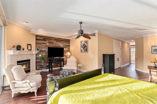 bedroom featuring a textured ceiling, crown molding, dark hardwood / wood-style flooring, a tiled fireplace, and ceiling fan