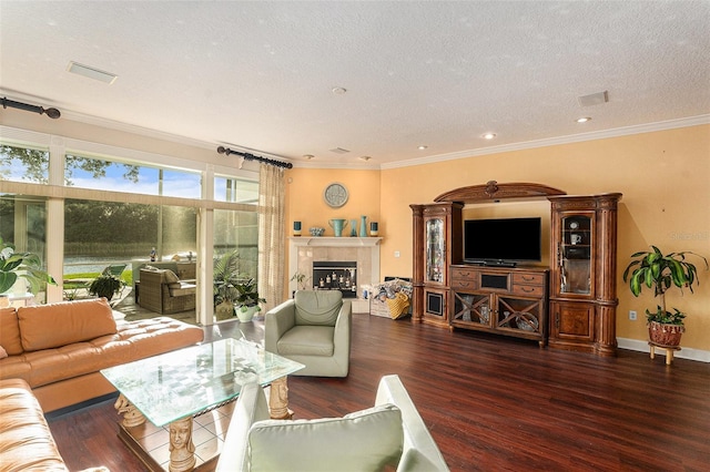 living room with dark wood-type flooring, a textured ceiling, a tiled fireplace, and ornamental molding