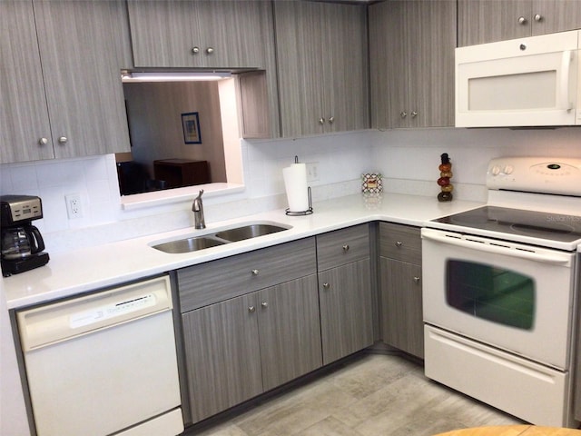 kitchen with light countertops, decorative backsplash, gray cabinetry, a sink, and white appliances