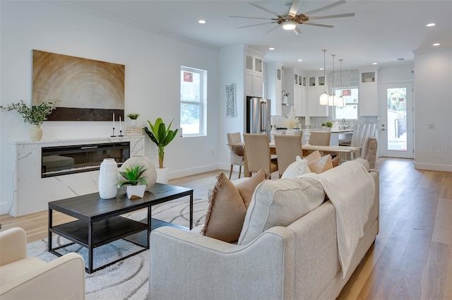 living room featuring light wood-type flooring, a healthy amount of sunlight, and crown molding