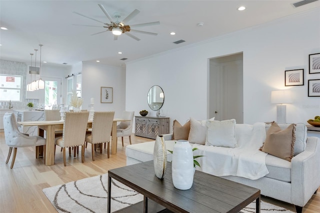 living room with light wood-type flooring, ceiling fan, crown molding, and sink