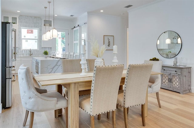 dining space featuring a barn door, light hardwood / wood-style flooring, and crown molding